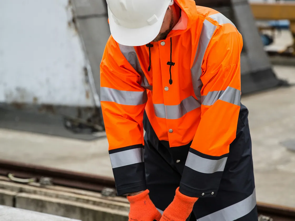 Opérateur en veste haute visibilité orange travaillant sur une structure métallique